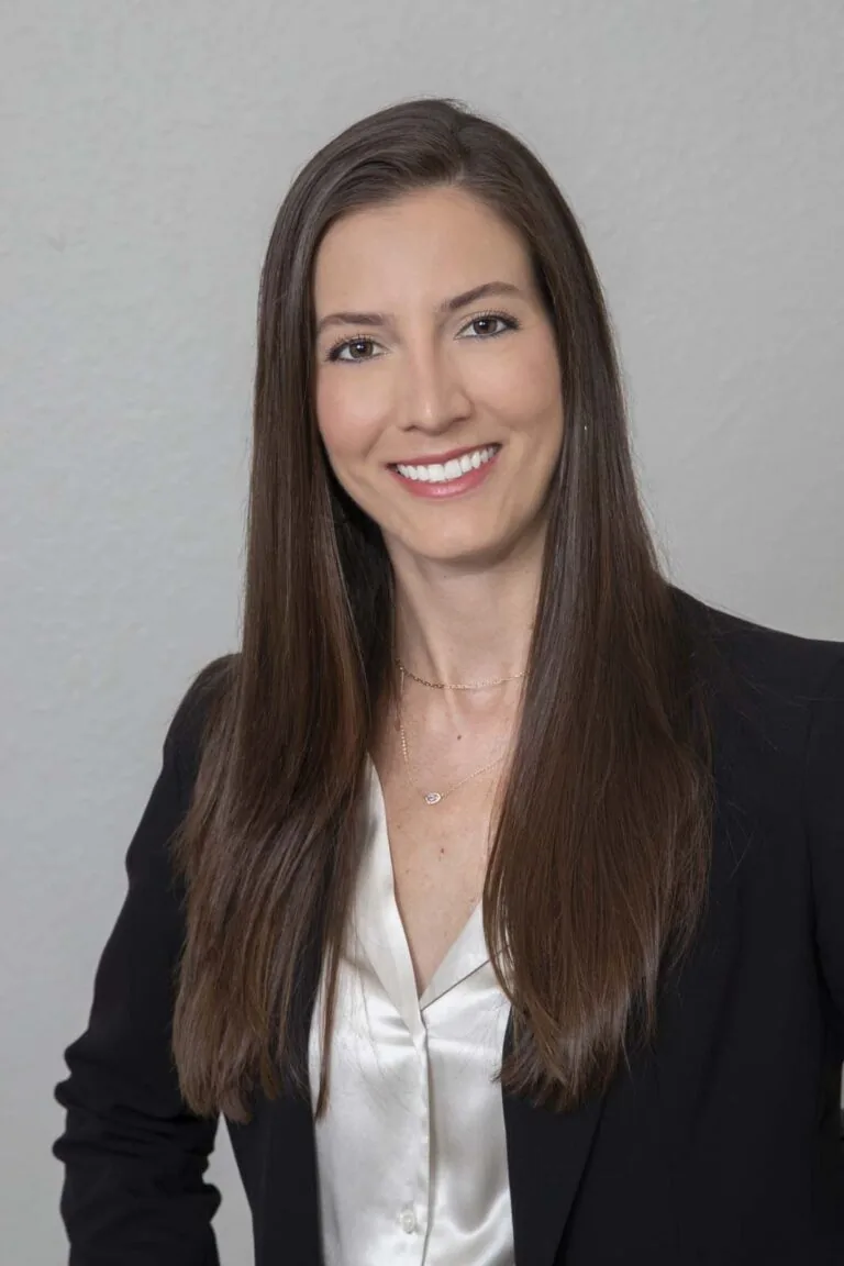The image shows Dr. Andrea Emmerich, a dental professional wearing a black blazer over a white blouse, with long, straight brown hair.