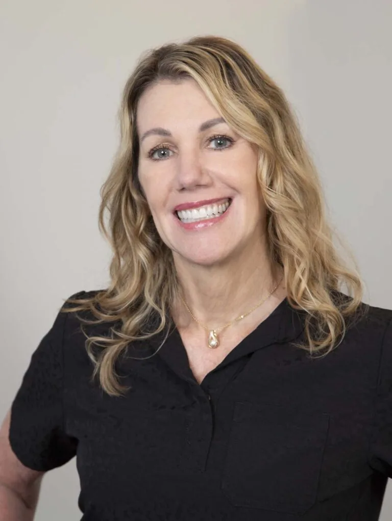 The image depicts Barbara (Barb) Thomas, a person with long, wavy blonde hair, wearing a black shirt and a necklace with a pendant.